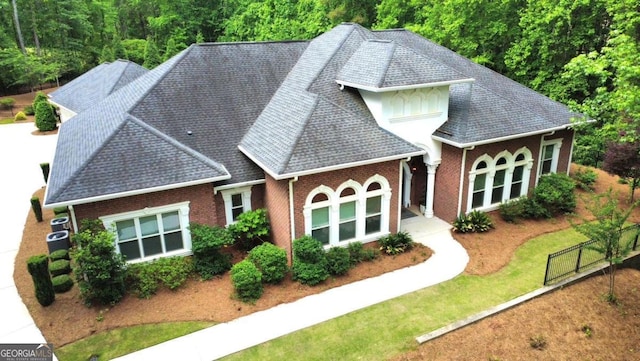 back of house with roof with shingles, a yard, and brick siding