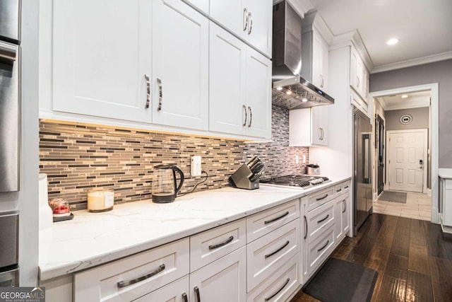 kitchen with wall chimney range hood, decorative backsplash, appliances with stainless steel finishes, white cabinets, and ornamental molding