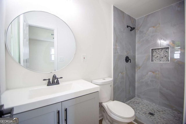 full bathroom featuring toilet, a tile shower, and vanity