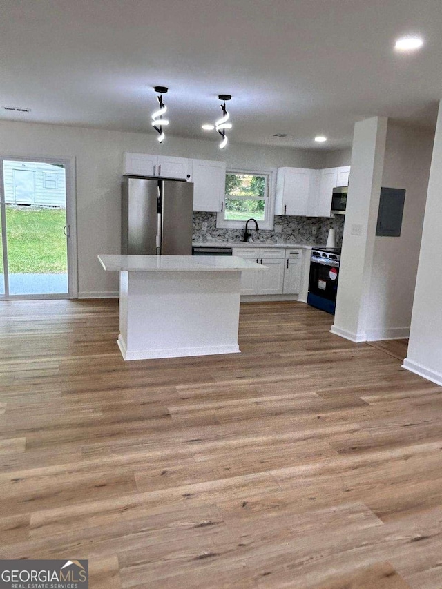 kitchen with decorative backsplash, baseboards, light wood-type flooring, white cabinetry, and stainless steel appliances