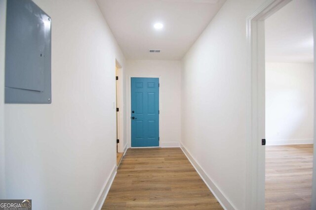 corridor featuring baseboards, electric panel, light wood finished floors, and visible vents