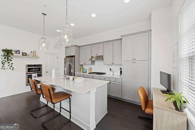 kitchen featuring under cabinet range hood, appliances with stainless steel finishes, gray cabinetry, and dark wood-type flooring