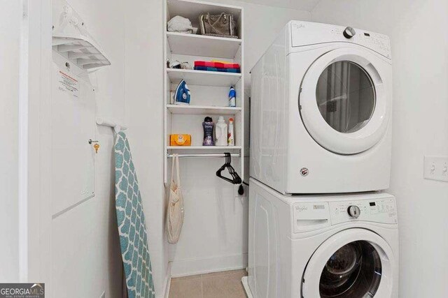 washroom featuring stacked washer / drying machine, tile patterned flooring, baseboards, and laundry area