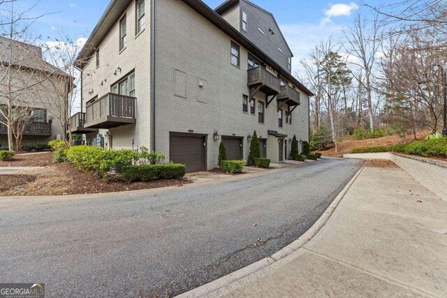 view of side of property featuring an attached garage, brick siding, a balcony, and driveway