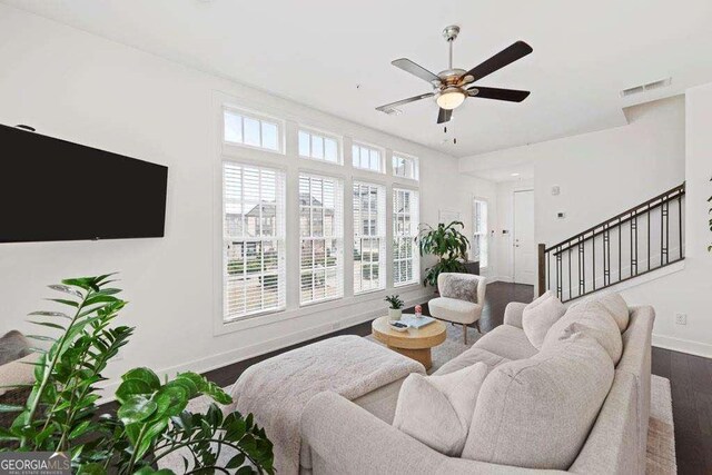 living area featuring a ceiling fan, dark wood-style flooring, visible vents, baseboards, and stairs