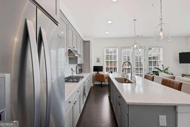 kitchen featuring dark wood-style flooring, appliances with stainless steel finishes, a sink, gray cabinets, and under cabinet range hood