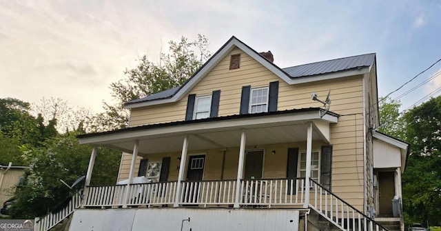 country-style home with a porch, stairs, a chimney, and metal roof
