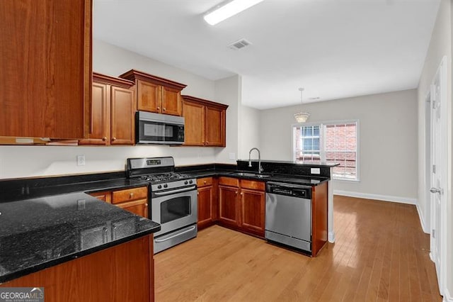 735 Scenic Creek Dr, Lawrenceville, GA 30046 - kitchen featuring appliances with stainless steel finishes, a peninsula, brown cabinetry, light wood finished floors, and dark stone countertops