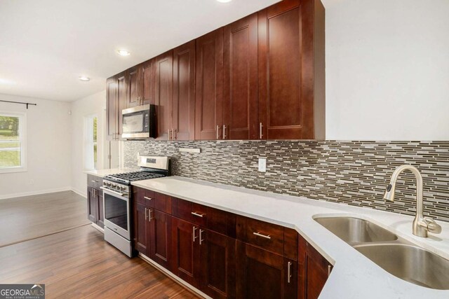 kitchen featuring appliances with stainless steel finishes, a sink, light countertops, tasteful backsplash, and dark wood-style floors