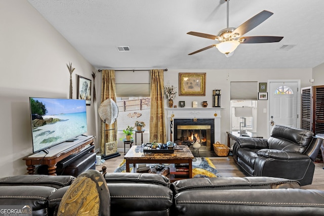 living room with a premium fireplace, ceiling fan, visible vents, and wood finished floors