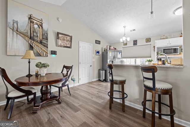 dining space featuring a textured ceiling, a notable chandelier, wood finished floors, and vaulted ceiling