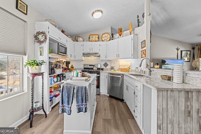 kitchen featuring under cabinet range hood, white cabinets, a sink, light wood-style flooring, and appliances with stainless steel finishes