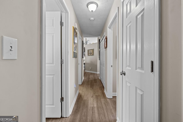 corridor with baseboards, light wood finished floors, and a textured ceiling