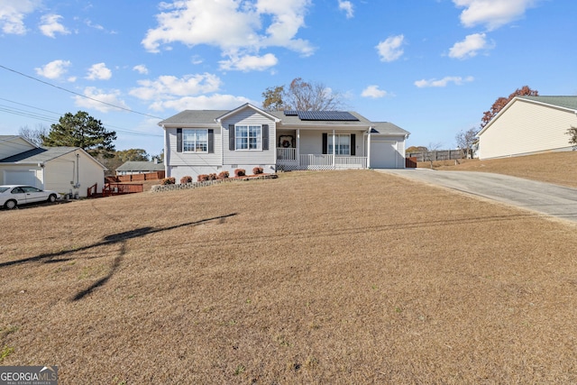 ranch-style home with a garage, covered porch, a front yard, roof mounted solar panels, and driveway