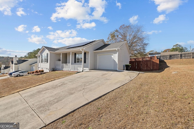 single story home with an attached garage, fence, roof mounted solar panels, a porch, and driveway