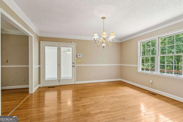 unfurnished dining area with ornamental molding, baseboards, a textured ceiling, a chandelier, and light wood finished floors