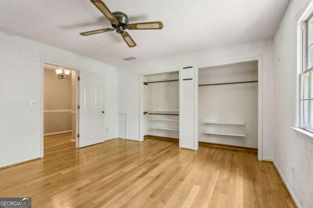 unfurnished bedroom featuring visible vents, wood finished floors, two closets, baseboards, and a ceiling fan