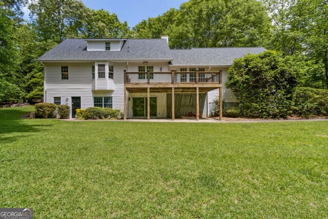 rear view of house featuring a wooden deck, a patio, a chimney, a shingled roof, and a yard