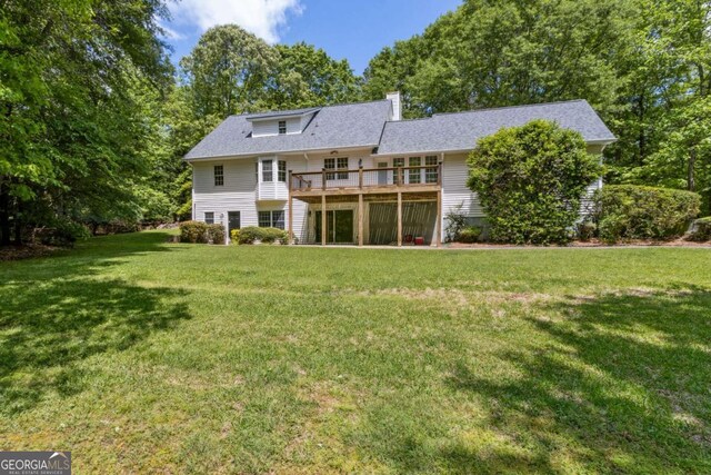 rear view of property featuring a lawn, a wooden deck, and a chimney