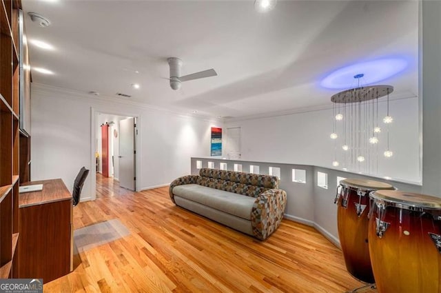 living area with ornamental molding, wood finished floors, a ceiling fan, and baseboards
