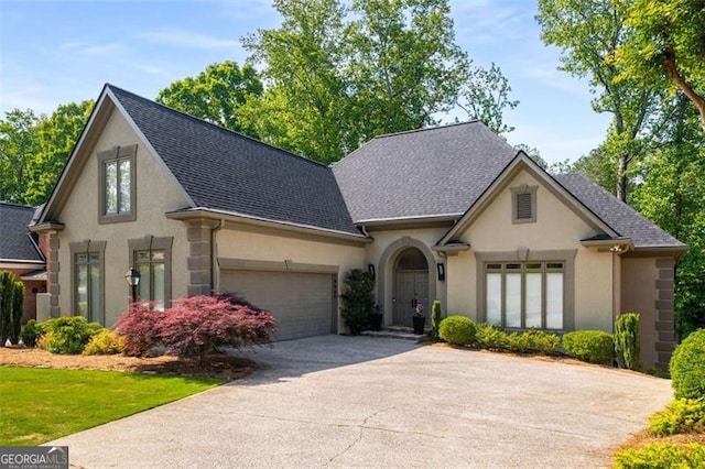 french country inspired facade featuring stucco siding, concrete driveway, an attached garage, and a shingled roof