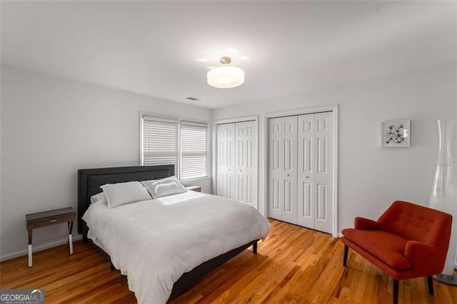 bedroom with two closets, light wood finished floors, and baseboards