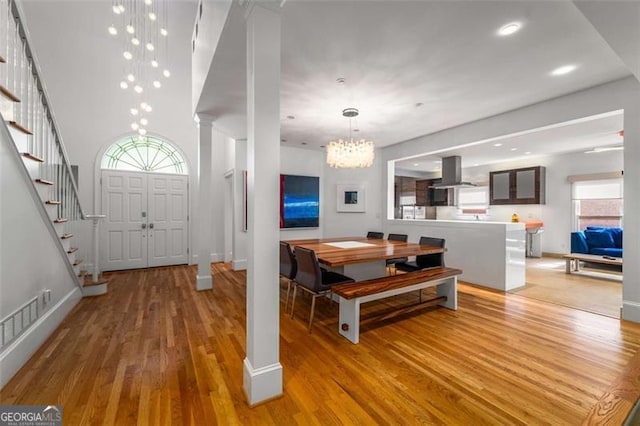 dining area featuring a chandelier, light wood-style floors, stairs, baseboards, and decorative columns