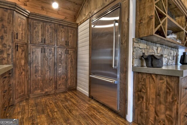 kitchen with wood walls, dark wood finished floors, vaulted ceiling, and stainless steel built in refrigerator