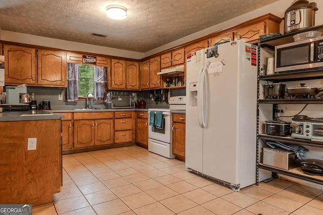 kitchen featuring white appliances, a textured ceiling, under cabinet range hood, brown cabinets, and a sink
