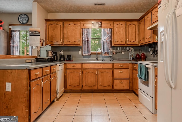 kitchen featuring brown cabinetry, visible vents, a peninsula, white appliances, and a sink
