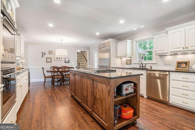 kitchen featuring white cabinets, dark countertops, a sink, stainless steel appliances, and ornamental molding