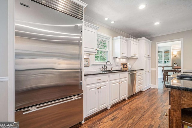kitchen with a sink, ornamental molding, stainless steel appliances, and white cabinets