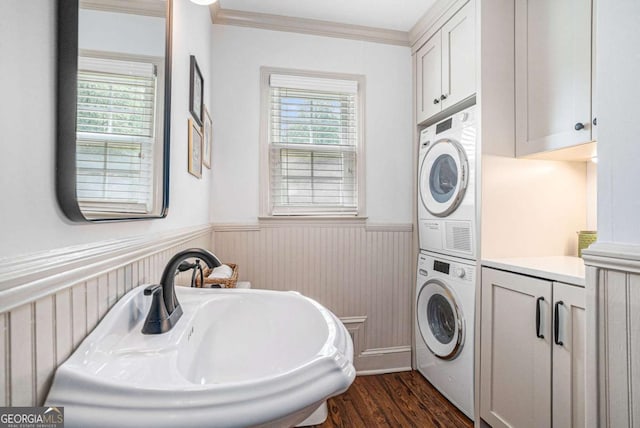 clothes washing area featuring cabinet space, stacked washer / drying machine, dark wood finished floors, and a wainscoted wall