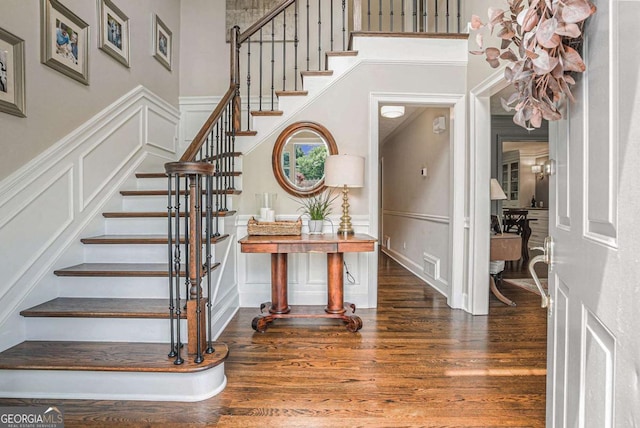 foyer entrance featuring visible vents, a decorative wall, stairway, and wood finished floors