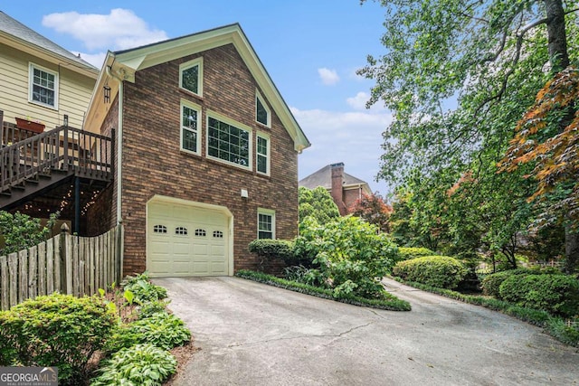 view of property exterior with fence, an attached garage, concrete driveway, and brick siding