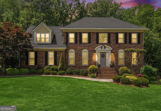 colonial house featuring roof with shingles, a front lawn, and brick siding