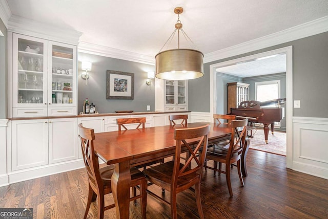 dining space featuring wainscoting, dark wood-style flooring, ornamental molding, and a decorative wall
