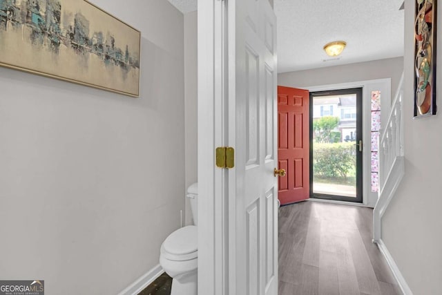 foyer entrance with baseboards, a textured ceiling, and wood finished floors