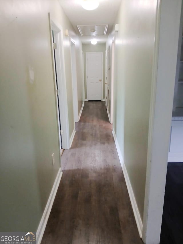 corridor with baseboards, wood finished floors, and attic access