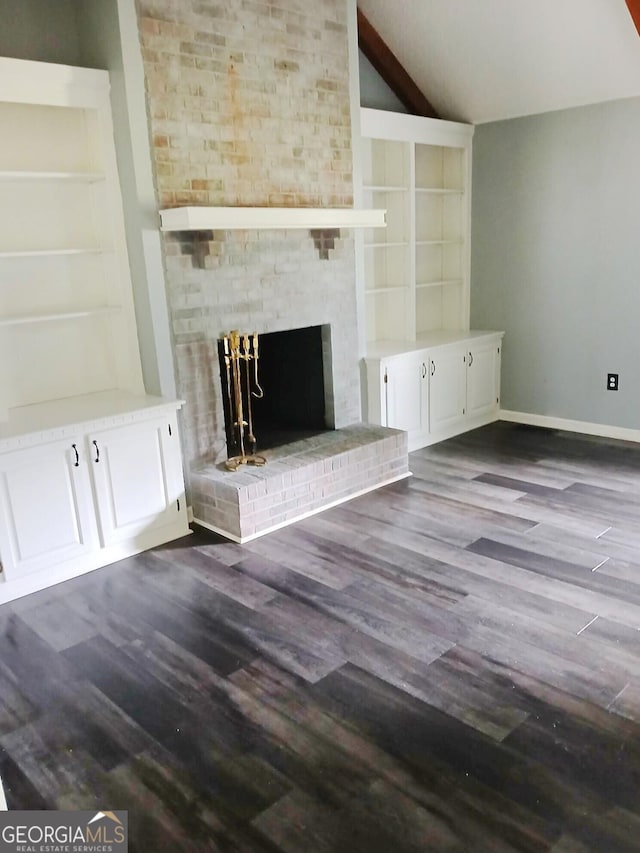 unfurnished living room featuring a fireplace, baseboards, built in shelves, dark wood finished floors, and vaulted ceiling