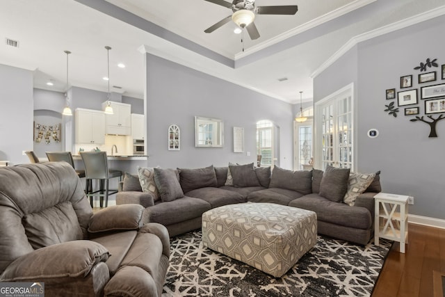 living area with visible vents, crown molding, baseboards, a ceiling fan, and dark wood finished floors