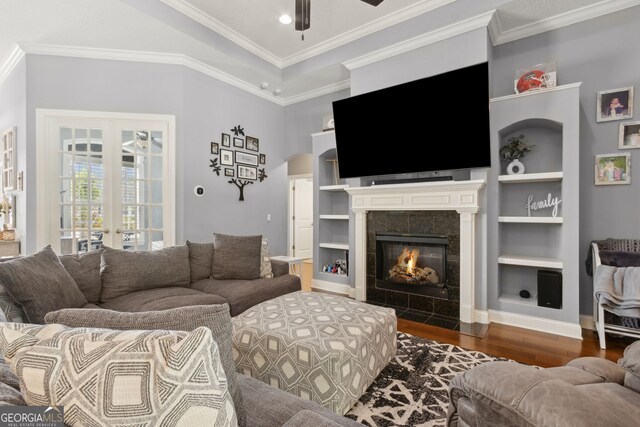 living area featuring built in features, a ceiling fan, baseboards, wood finished floors, and a tile fireplace