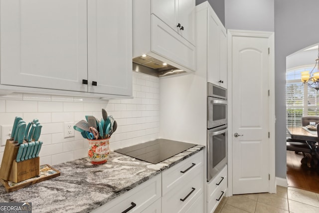 kitchen with light stone countertops, light tile patterned floors, black electric stovetop, a chandelier, and white cabinetry