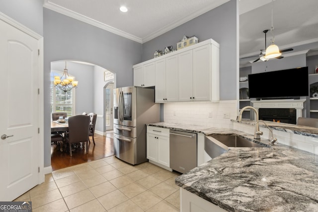 kitchen featuring arched walkways, appliances with stainless steel finishes, ornamental molding, and a sink