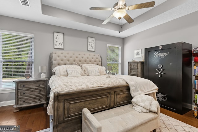 bedroom with baseboards, wood-type flooring, a tray ceiling, and visible vents