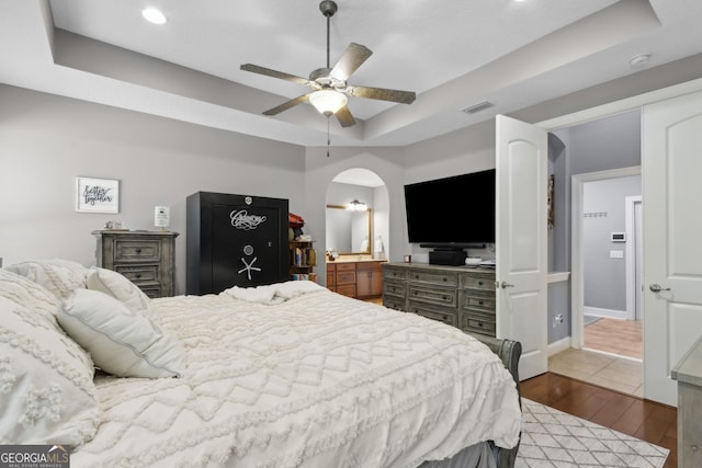 bedroom with arched walkways, dark wood finished floors, recessed lighting, a tray ceiling, and visible vents