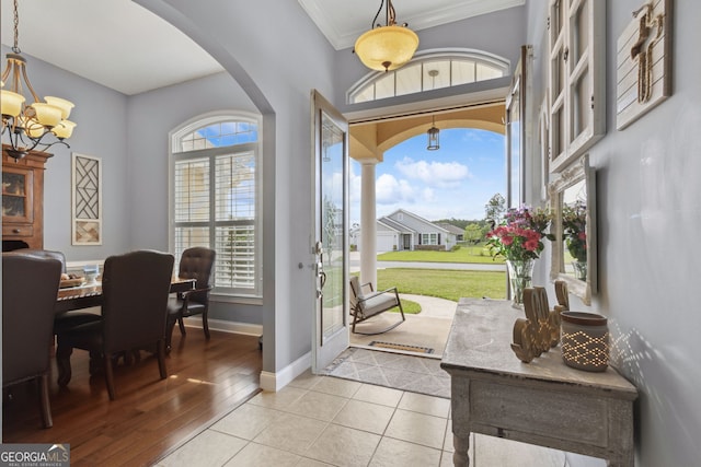 entryway featuring crown molding, arched walkways, baseboards, light wood finished floors, and an inviting chandelier