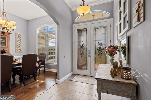 foyer featuring french doors, arched walkways, baseboards, a notable chandelier, and ornamental molding