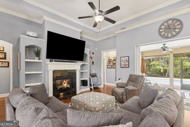 living area with ceiling fan, built in features, a fireplace, wood finished floors, and baseboards