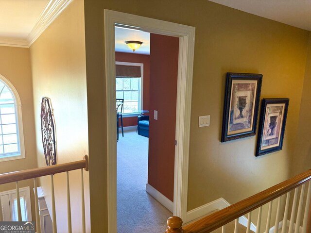 hallway featuring baseboards, ornamental molding, carpet, and an upstairs landing